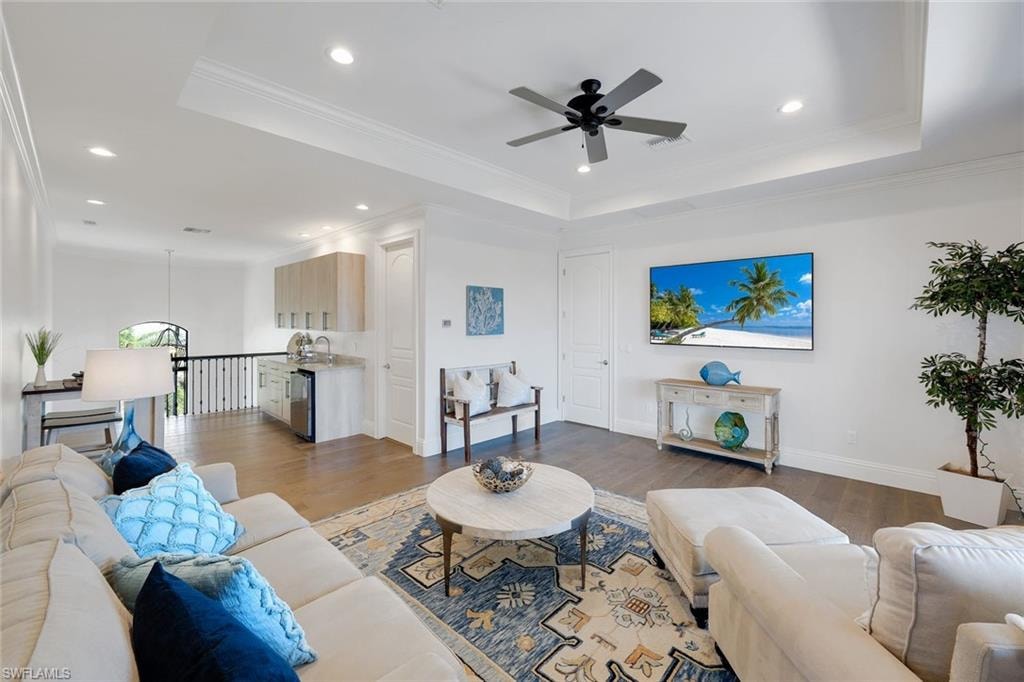 Living area featuring crown molding, a ceiling fan, wood finished floors, recessed lighting, and a raised ceiling