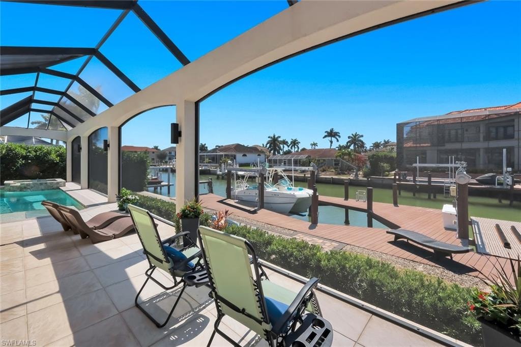View of patio with a sunroom, a boat dock, a pool with connected hot tub, and a water view