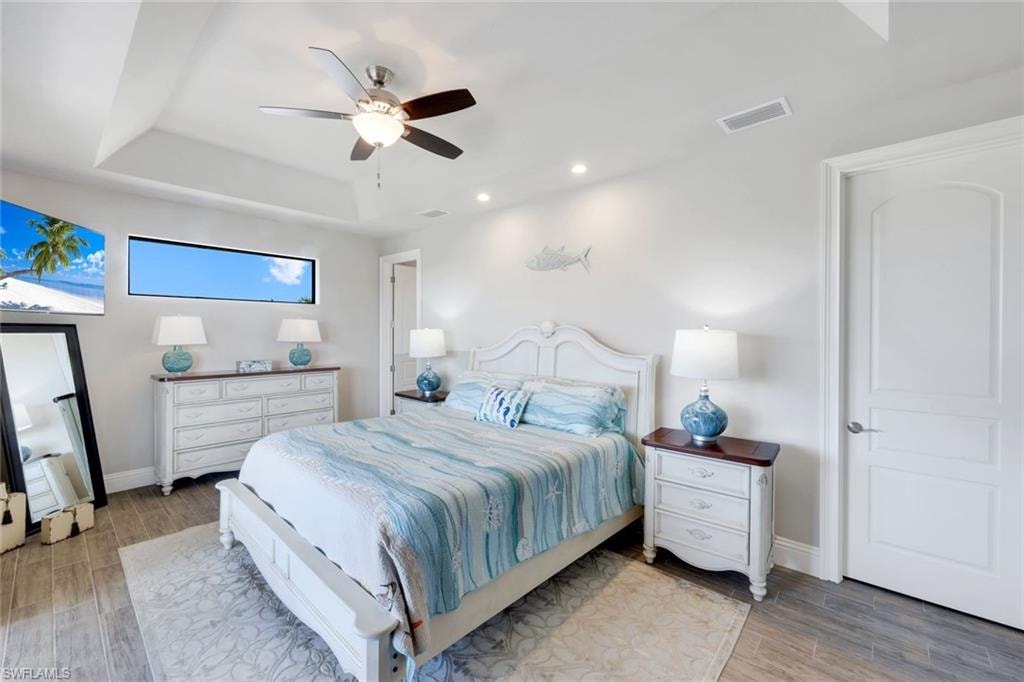 Bedroom with wood tiled floors, a ceiling fan, recessed lighting, and a raised ceiling