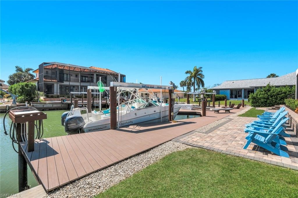 Dock area featuring a water view, boat lift, a lawn, and a patio area