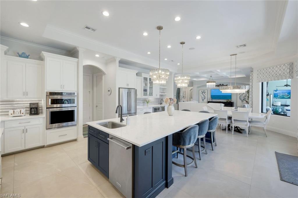 Kitchen featuring two tone cabinetry, backsplash, a large island, light stone counters, and stainless steel appliances