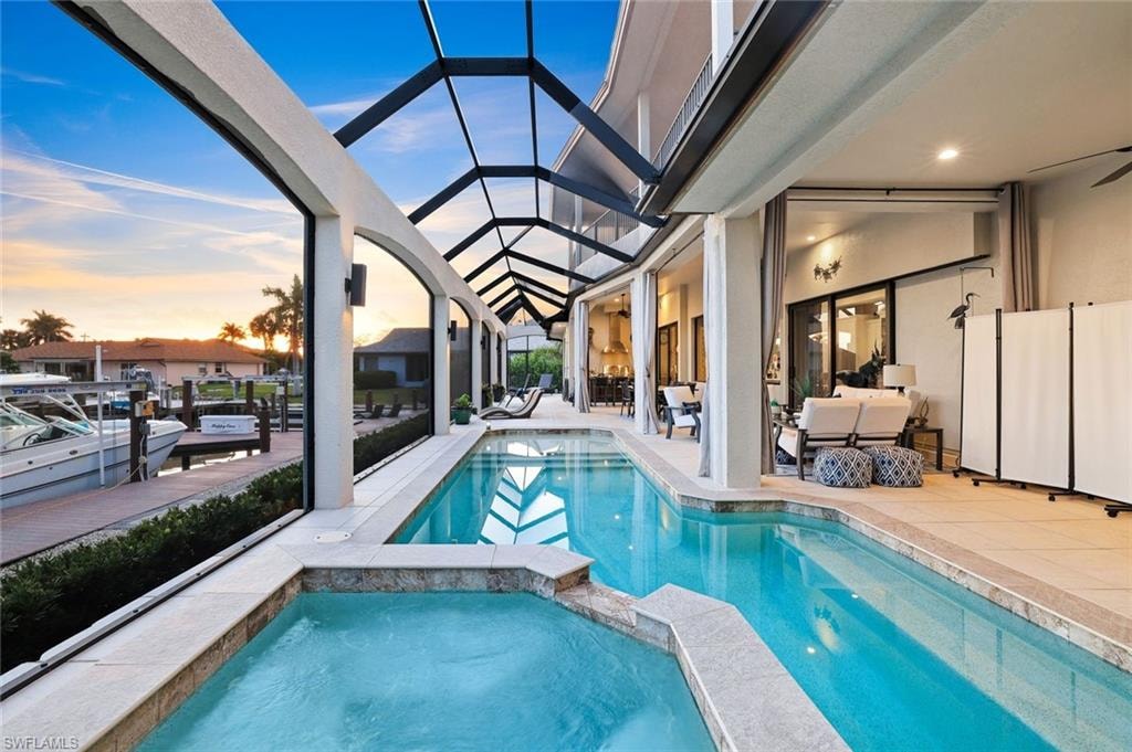 Pool at dusk with a sunroom, a patio, a pool with connected hot tub, glass enclosure, and an outdoor lounge area