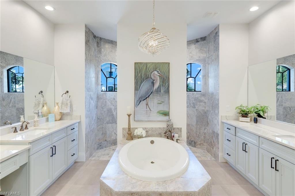 Bathroom featuring a bath, walk in shower, two vanities, and suspended lighting