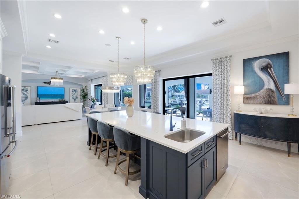 Kitchen with light stone countertops, open floor plan, high quality fridge, a large island, and crown molding