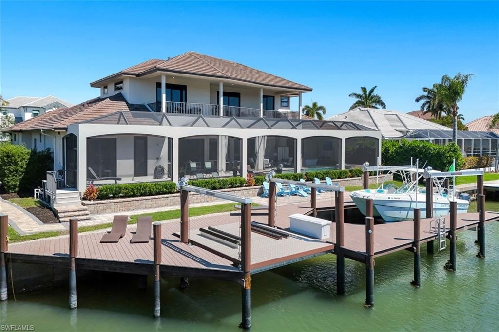 Dock featuring a water view, a sunroom, boat lift, and a balcony
