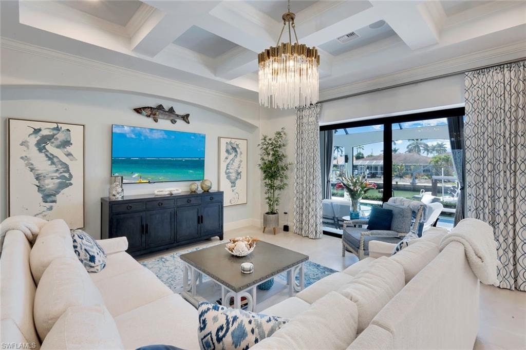 Living area with coffered ceiling, ornamental molding, and a chandelier