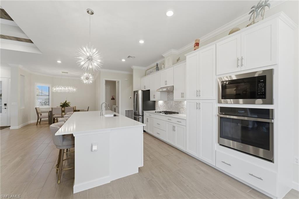 Kitchen featuring a kitchen bar, stainless steel appliances, a kitchen island with sink, ornamental molding, and white cabinetry