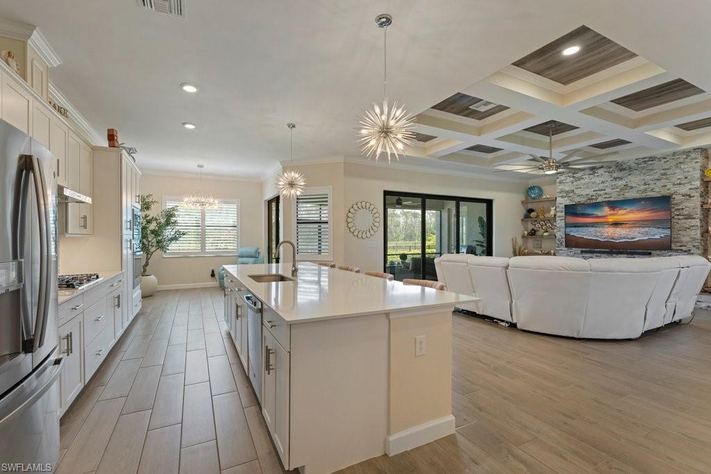 Kitchen with ornamental molding, white cabinetry, wood tiled floors, stainless steel appliances, and an island with sink