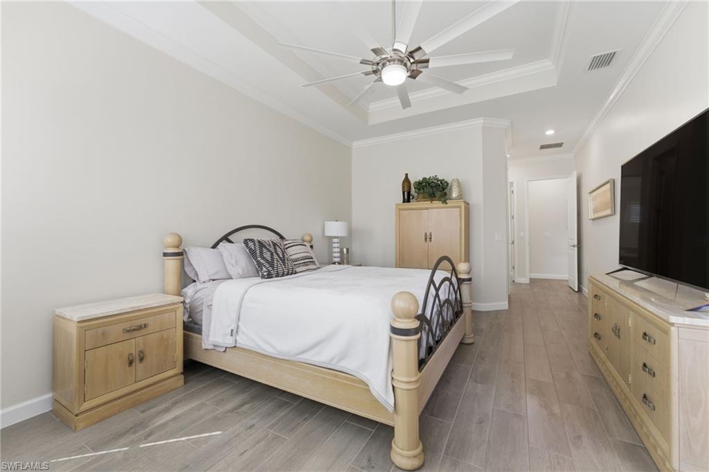 Bedroom with wood tiled floors, a ceiling fan, ornamental molding, and a raised ceiling