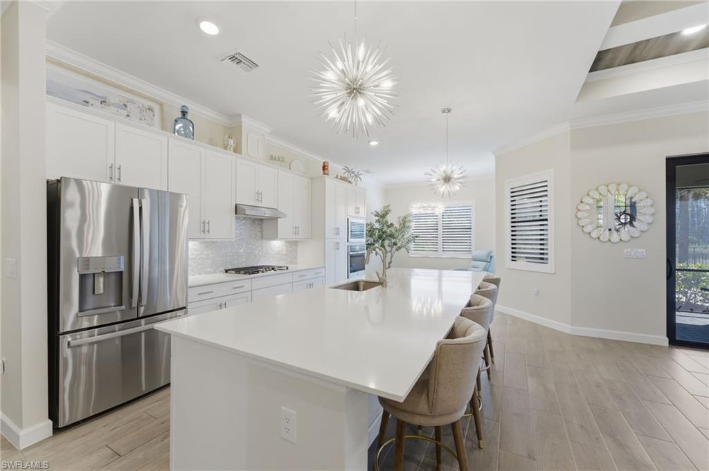 Kitchen with stainless steel appliances, light wood-style floors, white cabinets, a chandelier, and crown molding