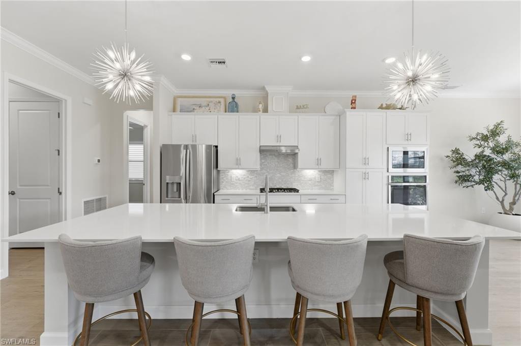 Kitchen with suspended lighting, white cabinetry, a spacious island, stainless steel appliances, and crown molding