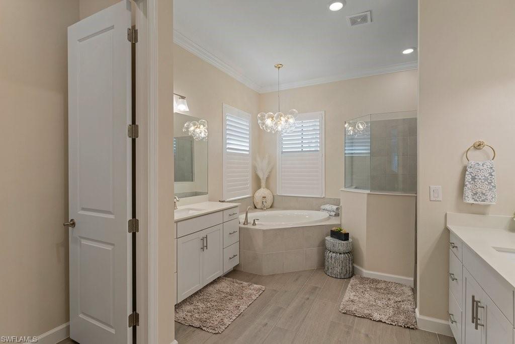Full bathroom featuring crown molding, light wood finished floors, a bath, two vanities, and a walk in shower
