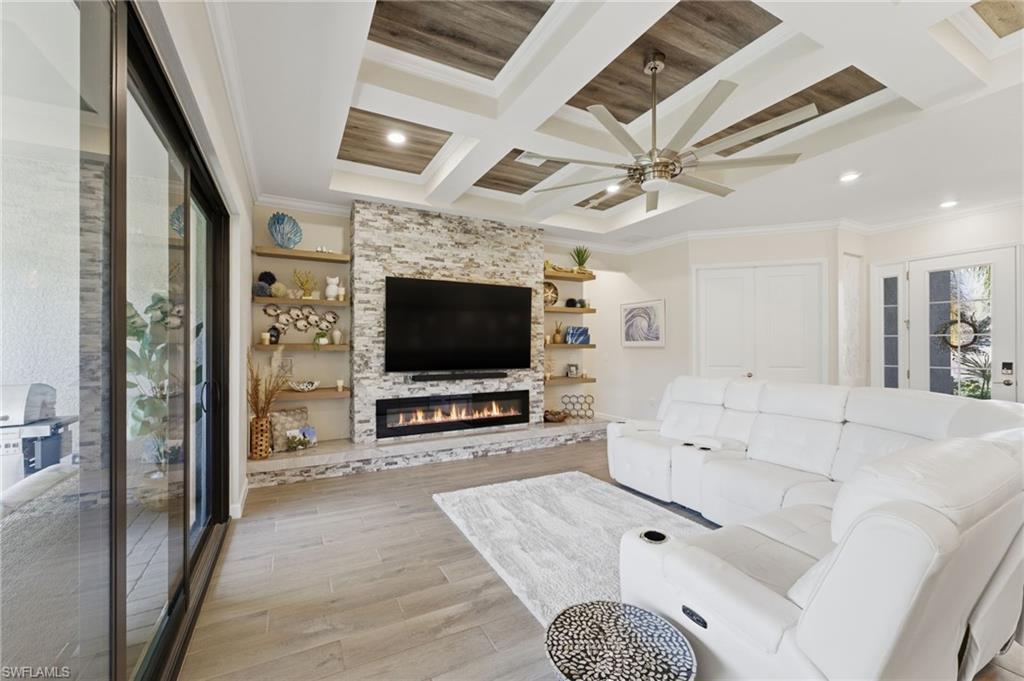 Living area featuring coffered ceiling, light wood-style floors, ornamental molding, ceiling fan, and a large fireplace