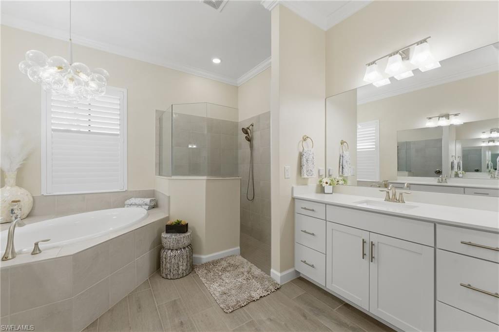 Bathroom with vanity, a walk in shower, a bath, suspended lighting, and ornamental molding