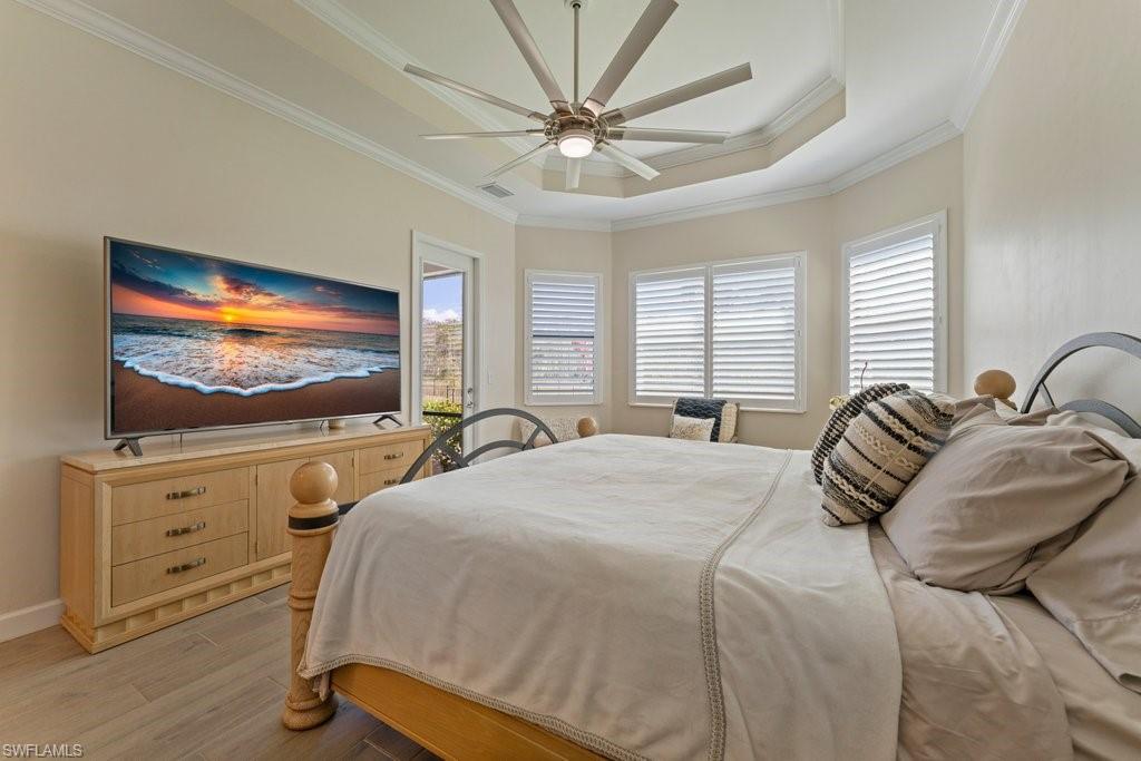 Bedroom with light wood finished floors, multiple windows, a ceiling fan, ornamental molding, and a raised ceiling