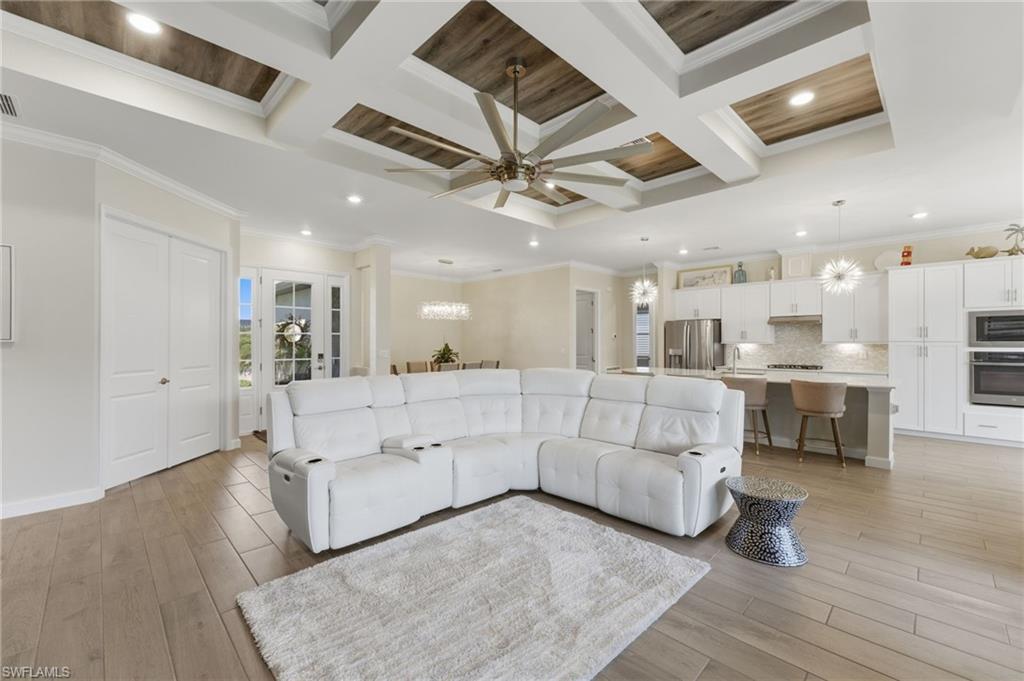 Living room with coffered ceiling, light wood-style floors, ornamental molding, a chandelier, and ceiling fan
