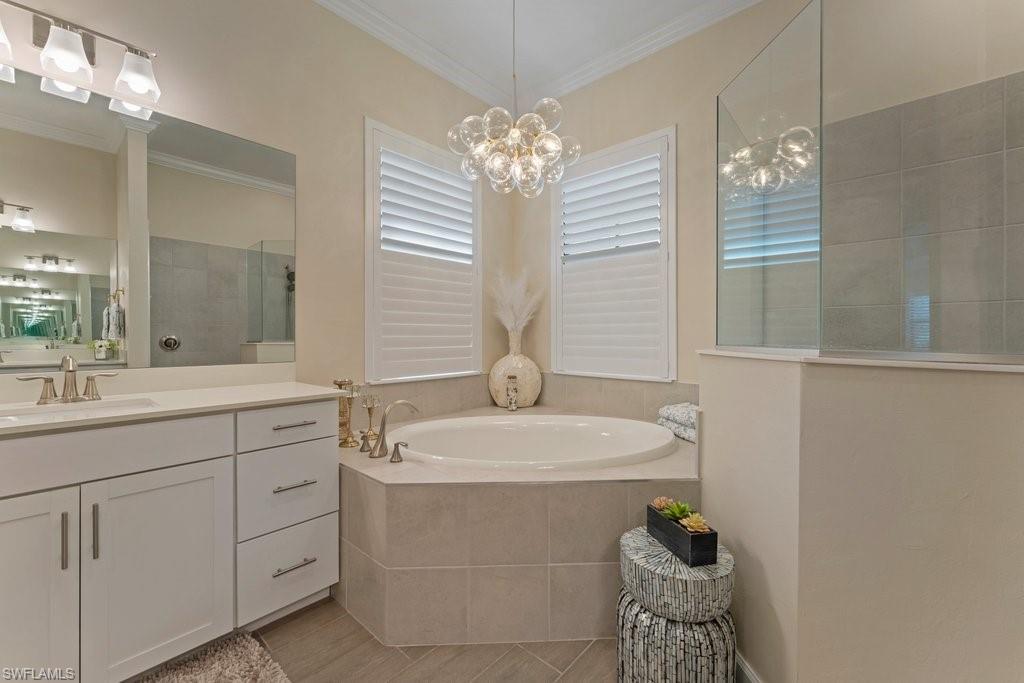 Bathroom featuring vanity, a garden tub, walk in shower, crown molding, and hanging lights