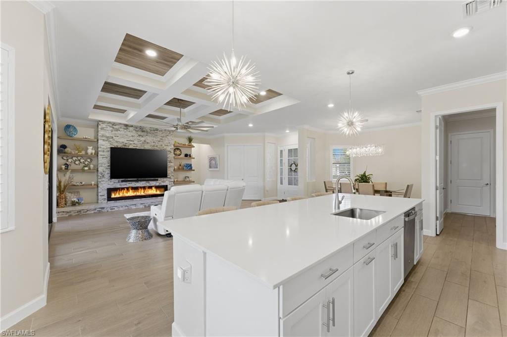 Kitchen featuring white cabinetry, a center island with sink, a chandelier, ornamental molding, and open floor plan