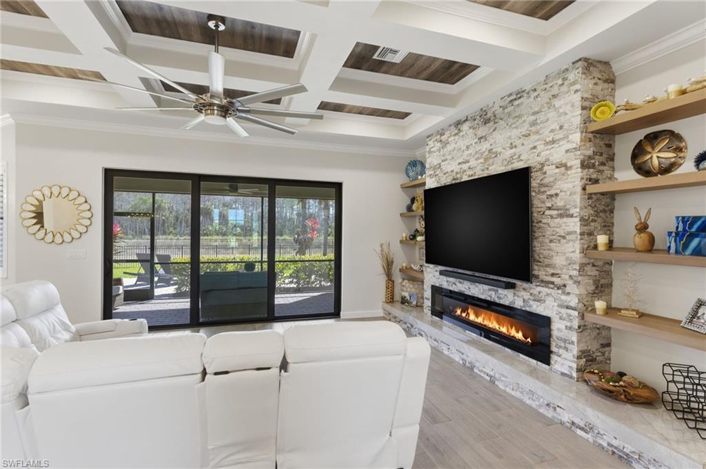 Living area featuring a fireplace, coffered ceiling, light wood finished floors, crown molding, and a ceiling fan