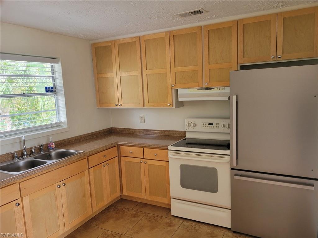 Kitchen featuring freestanding refrigerator, white range with electric cooktop, light wood finish cabinetry, a textured ceiling, and dark countertops