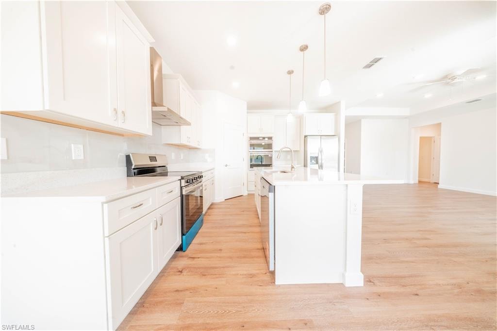 Kitchen with stainless steel appliances, light wood-style flooring, white cabinets, a ceiling fan, and a kitchen island with sink