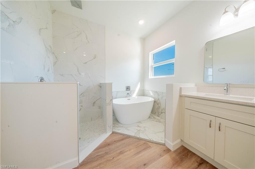 Full bathroom featuring a freestanding tub, a marble finish shower, vanity, light wood-type flooring, and recessed lighting