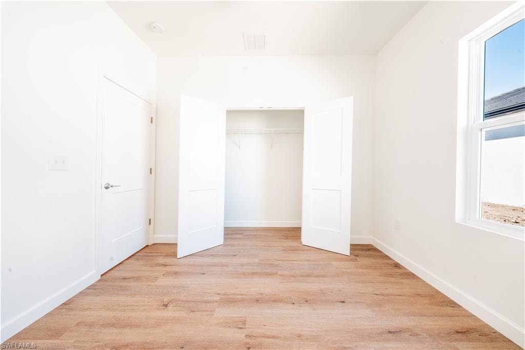 Unfurnished bedroom featuring light wood finished floors, multiple windows, and a closet