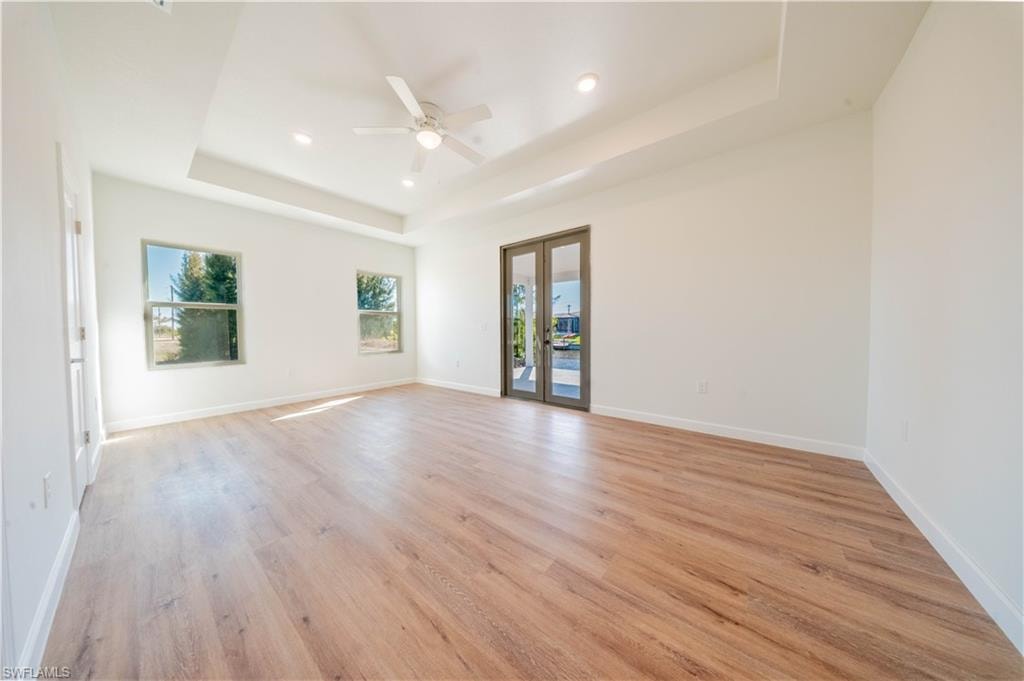 Spare room featuring ceiling fan, french doors, light wood-type flooring, recessed lighting, and a raised ceiling
