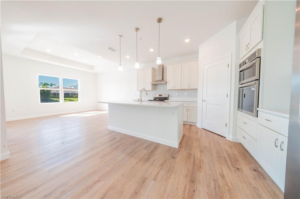 Kitchen featuring open floor plan, an island with sink, hanging light fixtures, white cabinetry, and light wood-type flooring