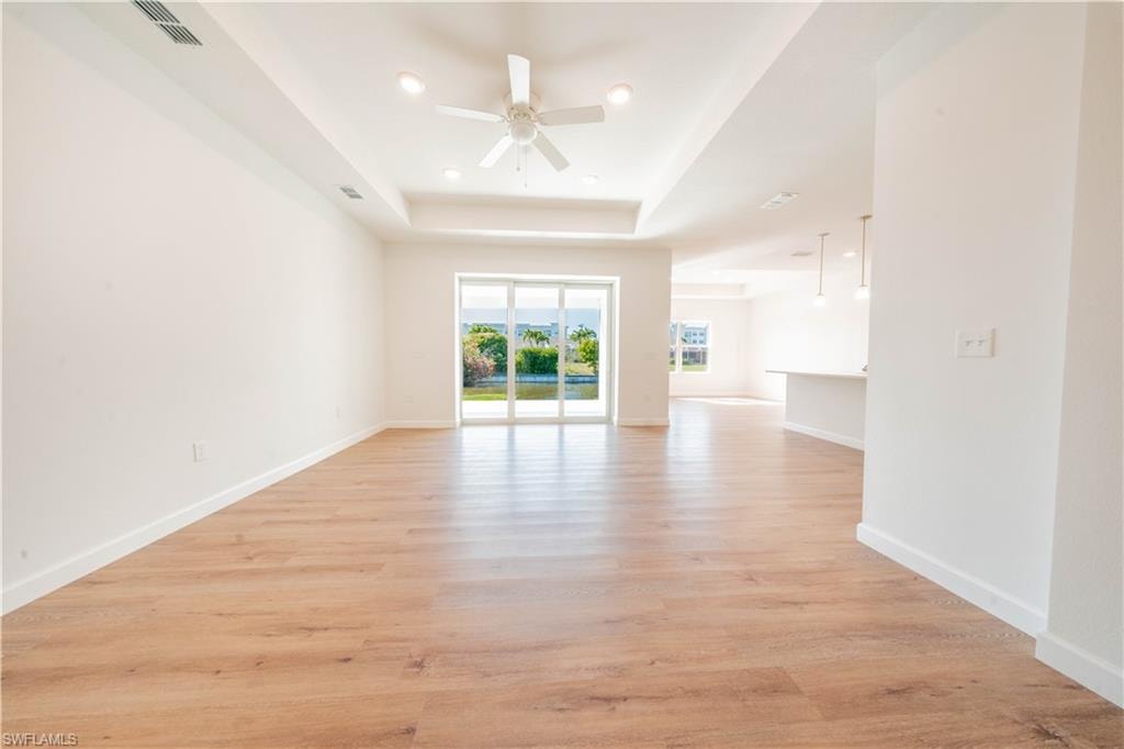 Empty room featuring a ceiling fan, light wood-style flooring, a raised ceiling, and recessed lighting