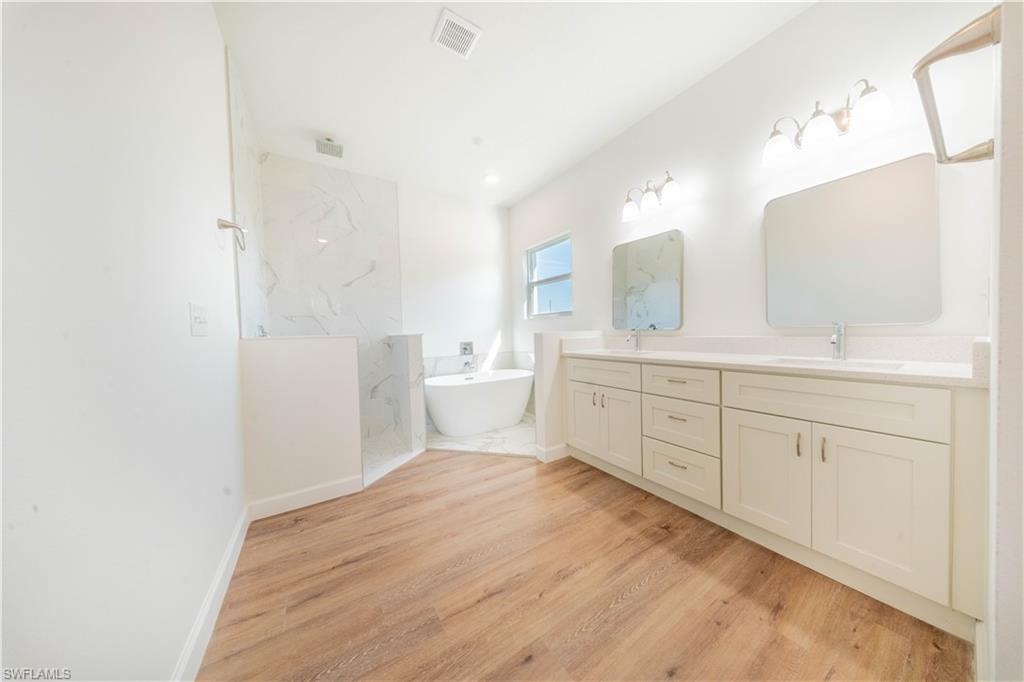 Bathroom with double vanity, a soaking tub, light wood finished floors, and a marble finish shower