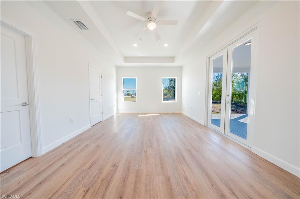 Unfurnished room featuring a tray ceiling, light wood finished floors, ceiling fan, french doors, and recessed lighting