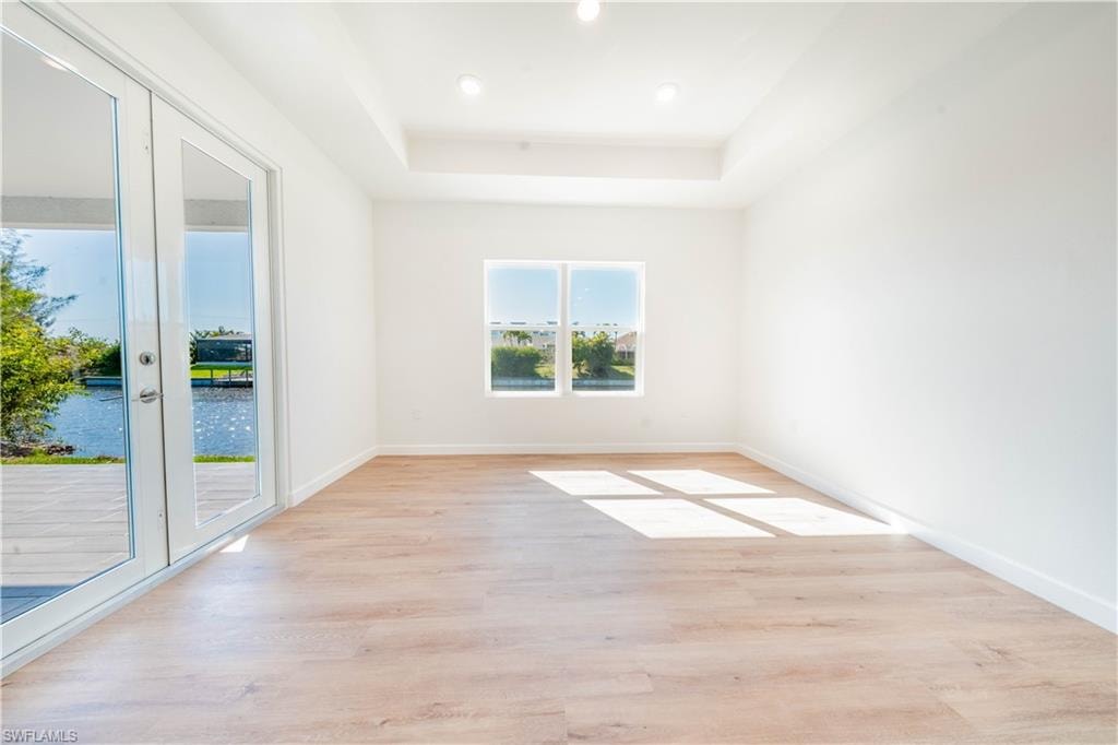 Empty room with light wood-style floors, a water view, a tray ceiling, and recessed lighting