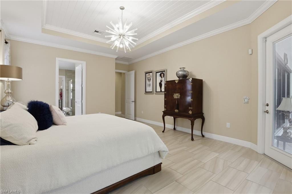 Bedroom featuring a raised ceiling, crown molding, access to outside, and a chandelier