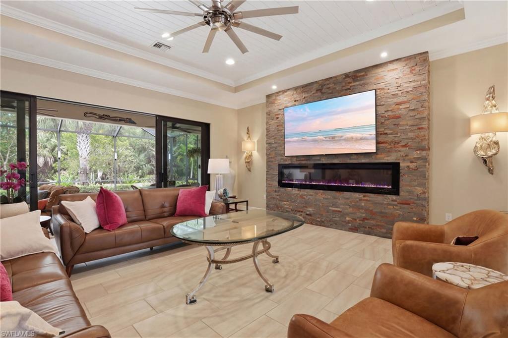 Living area featuring a ceiling fan, a stone fireplace, a wooden tray ceiling, recessed lighting, and crown molding