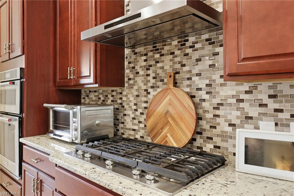 Kitchen featuring stainless steel appliances, tasteful backsplash, light stone counters, and bold wood finish cabinets