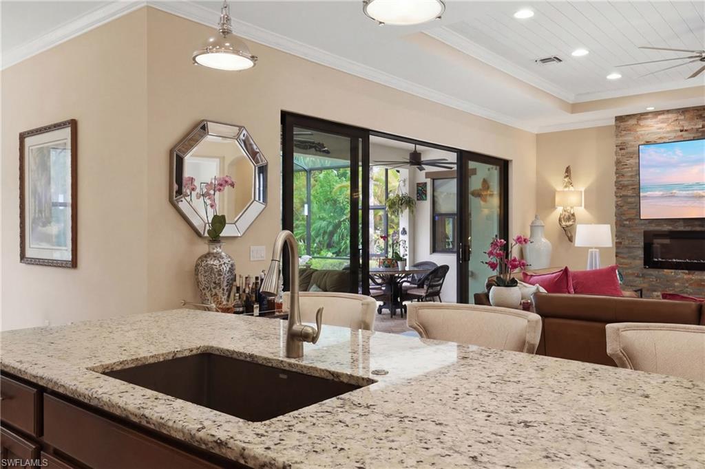 Kitchen with ceiling fan, crown molding, light stone countertops, a stone fireplace, and open floor plan