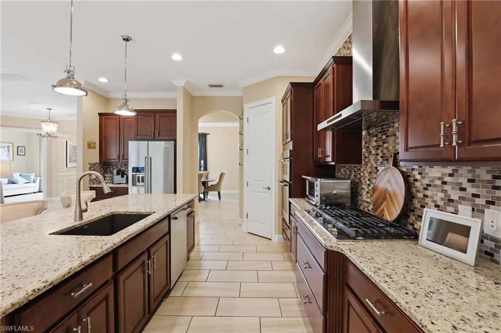 Kitchen featuring light stone countertops, backsplash, stainless steel appliances, arched walkways, and crown molding