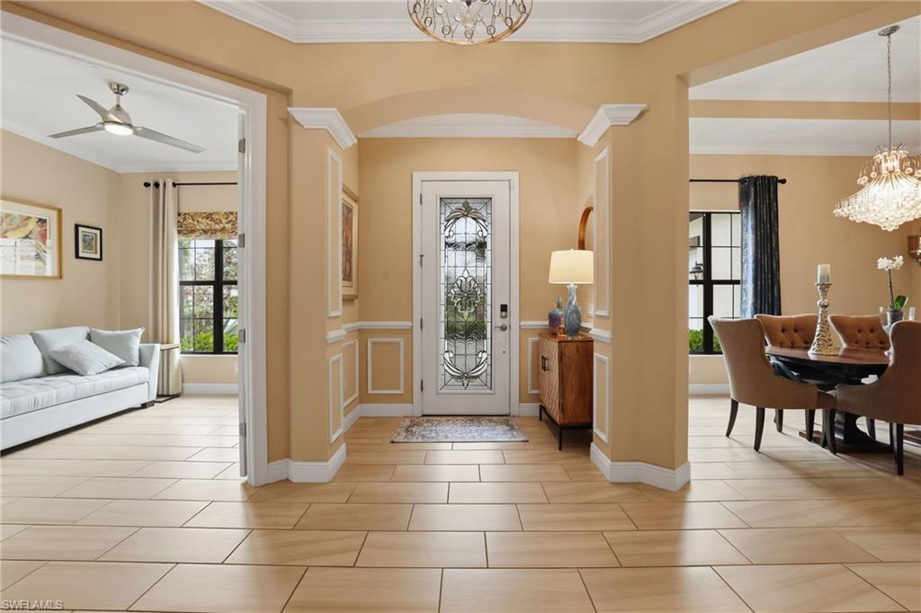Foyer entrance featuring suspended lighting, crown molding, a wainscoted wall, ceiling fan, and arched walkways