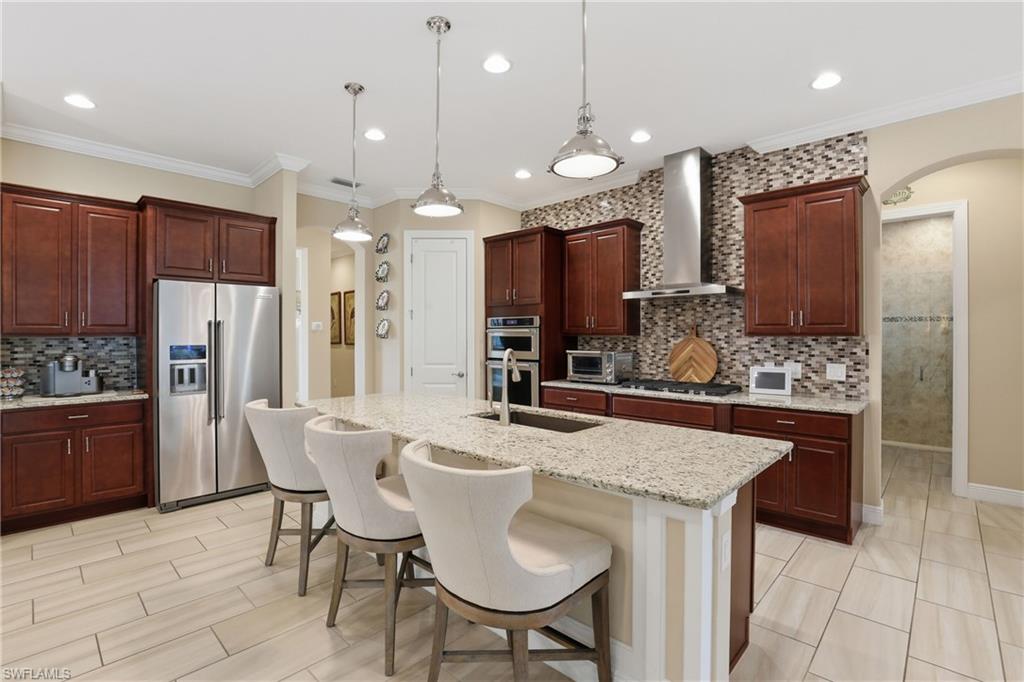 Kitchen with arched walkways, stainless steel appliances, a breakfast bar, tasteful backsplash, and ornamental molding