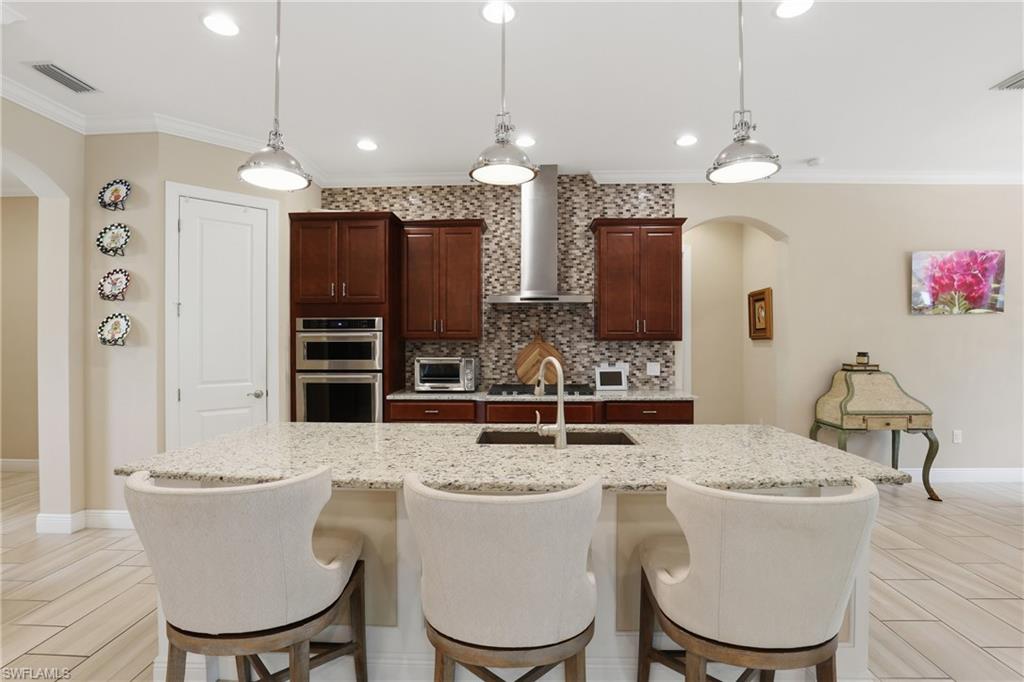 Kitchen featuring arched walkways, crown molding, wood finish floors, and light stone counters