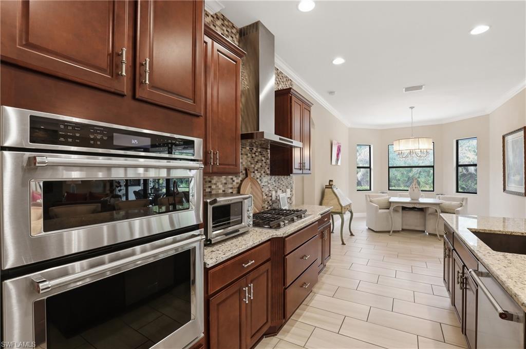 Kitchen with stainless steel appliances, light stone countertops, crown molding, tasteful backsplash, and hanging lights