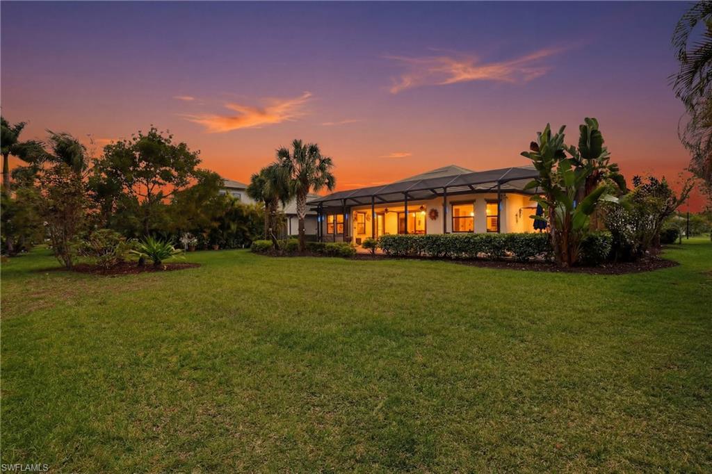 Back of house at dusk featuring glass enclosure, a sunroom, and a lawn