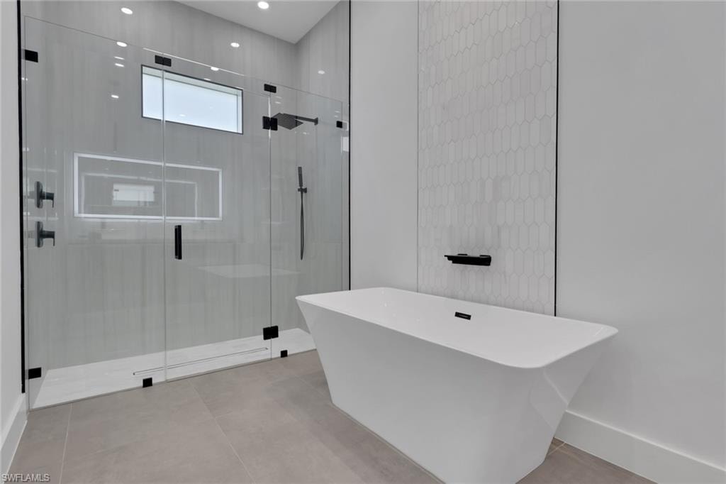 Contemporary bathroom featuring a freestanding soaking tub with a wall-mounted faucet, a glass-enclosed shower with matte black fixtures, an elongated hexagonal tile accent wall, and large format floor tiles