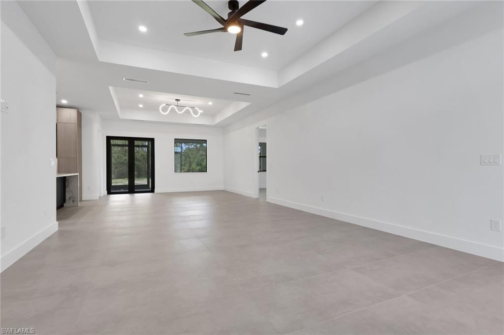 Spacious room featuring light gray tile flooring, white walls, and a tray ceiling with recessed lighting