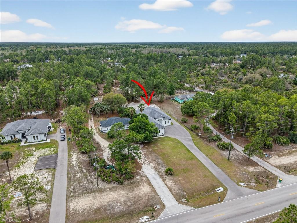 Aerial view showcasing a property with a light-colored exterior and dark roof, set among mature trees