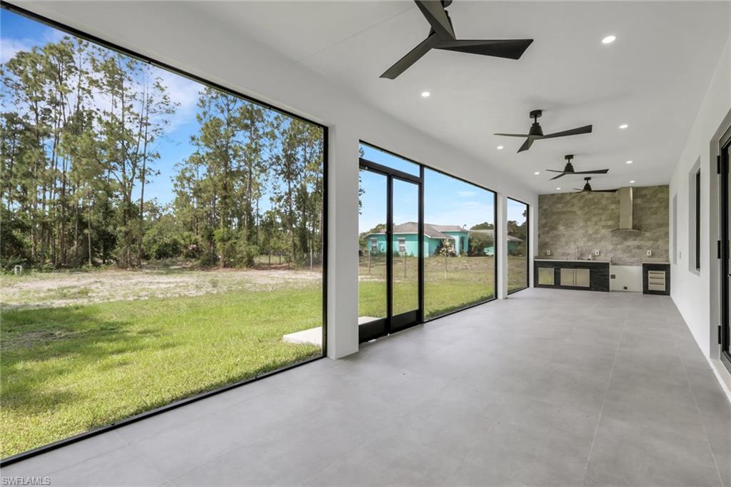 Expansive covered patio featuring large format tile flooring, black ceiling fans, recessed lighting, and an outdoor kitchen