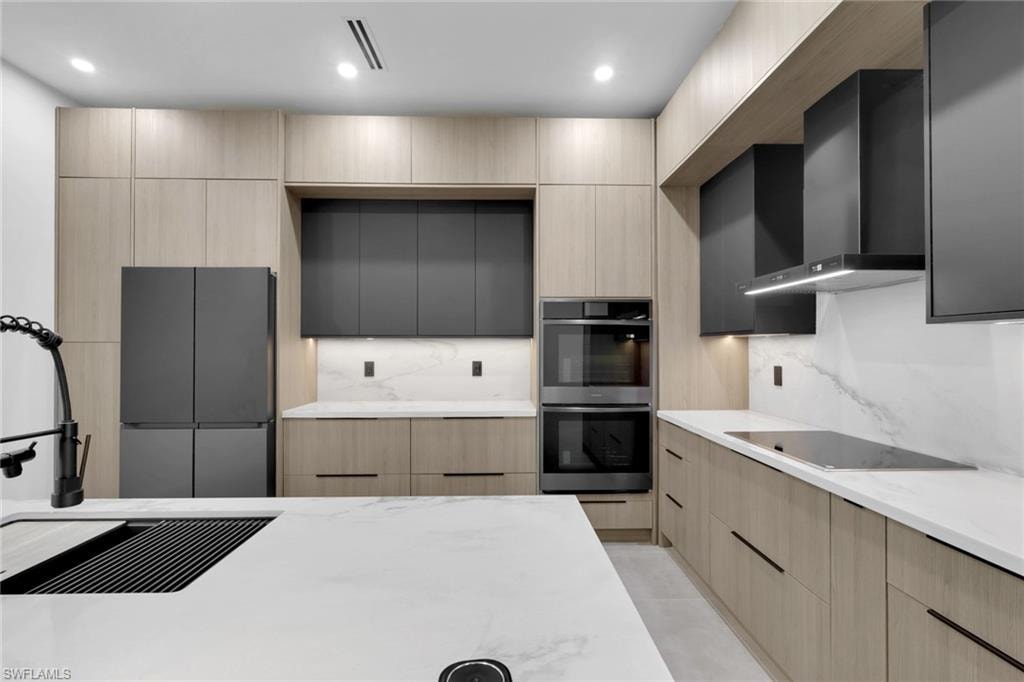 Modern kitchen featuring light wood-finish cabinetry, white countertops with natural veining, and integrated matte black appliances
