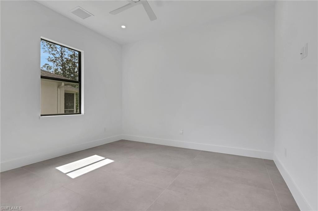 Bright room featuring large format tile flooring, a window with exterior tree-lined scenery, a ceiling fan, and recessed lighting