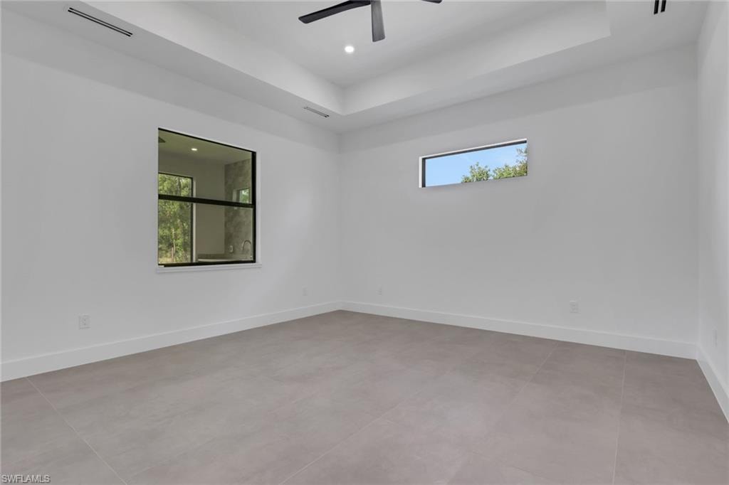 Spacious room featuring light-toned tile flooring, white walls, and a tray ceiling